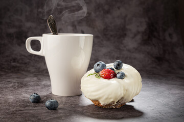 Tea in a white mug with a handle, a spoon, a cake with strawberries and blueberries on a gray background