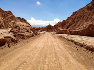 Fototapeta na wymiar Endless sandy road surrounded by rough rocks under blue sky on sunny day in Atacama desert