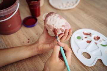 Close-up of girl painting clay mug. Woman coloring pottery in workshop with a paintbrush. Painter...