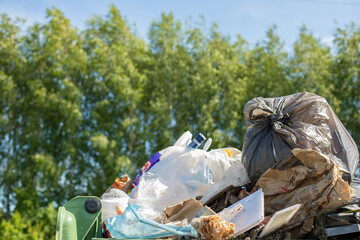Overflowing trash can, a green grove. Environmental pollution concept, human waste harmful to the...