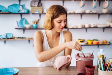 Hand dipping paintbrush into palette on wooden table. Finishing manufacturing procces of clay pottery production. Exclusive handmade products turquoise and royal blue bowls