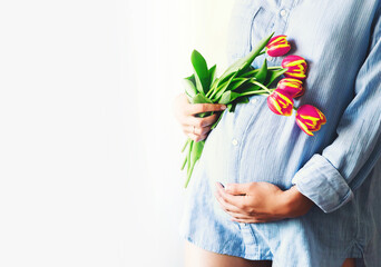 Young pregnant woman with tulips flowers holds hands on belly on a white background. Loving woman...