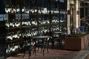 窓越しにワインの立ち並ぶ喫茶店のオープンカフェにある金属製の椅子とテーブル