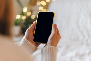 Cropped of woman's hands in white sweater holding mobile smart phone with blank screen of gadget at...