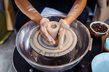 Close-up of the hands of a woman ceramist working with a potter's wheel in a cozy, bright workshop....
