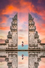Fototapeten Bali A girl is jumping in front of the Gate of Heaven with its reflection in the water during a stunning sunset. Pura Lempuyang is a must-visit place for tourists who want to strike a pose in Bali.  © Travel Wild
