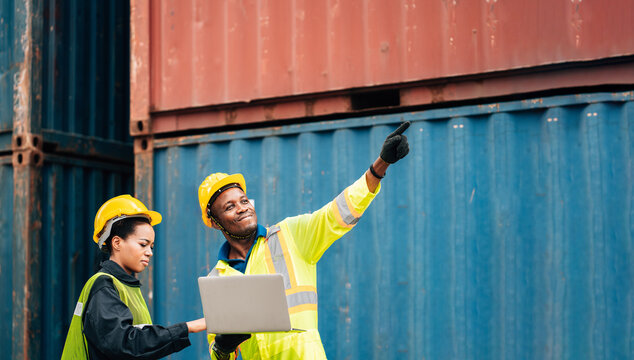 worker team man and woman in protective safety jumpsuit uniform with yellow hardhat and use laptop check container at cargo shipping warehouse. transportation import,export logistic industrial service