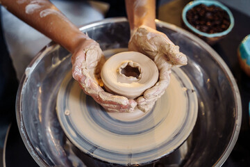 Close-up of the hands of a woman ceramist working with a potter's wheel in a cozy, bright workshop. A young experienced woman skillfully makes a mug, vase or plate. Creative people, pottery workshop