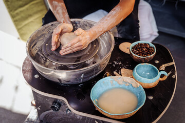 Close-up of the hands of a woman ceramist working with a potter's wheel in a cozy, bright workshop. A young experienced woman skillfully makes a mug, vase or plate. Creative people, pottery workshop