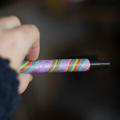 ballpoint pen in hand covered with polymer clay rainbow pattern