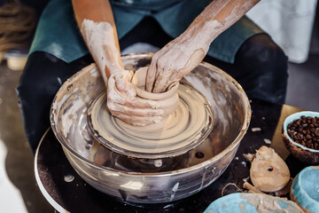 Close-up of the hands of a woman ceramist working with a potter's wheel in a cozy, bright workshop. A young experienced woman skillfully makes a mug, vase or plate. Creative people, pottery workshop