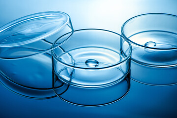 Clean glass petri dish with liquid drop inside over blue light background