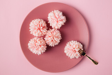 Flat lay view of five flowers  in the pink plate with golden fork. Minimal concept of eating quality, light food.
