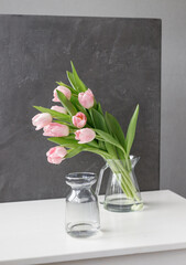 pink tulips in a large glass vase stand on the table, on a gray background, space for text, free space, floristry, florist, tulip bouquets, bouquet, valentine's day, international women's day,flowers