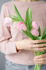 pink tulips with green leaves in a glass vase, a woman holds tulip buds in her hands, florist, floristry, gift, bouquet, bouquet for a girl, a bouquet of tulips, place for text, place for an inscript