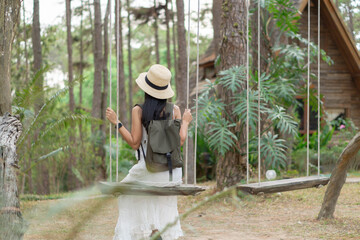 A female Asian tourist in white dress sits on a swing, and enjoys a vacation in pine forest at Doi Bo Luang, Chiang Mai, Thailand.