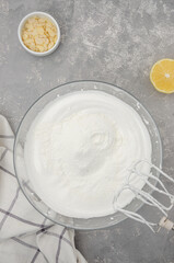 Cooking meringue Pavlova roll cake. Whipped egg whites with sugar and cornstarch in a bowl on a gray concrete background. Recipe step by step. Vertical, Top view.