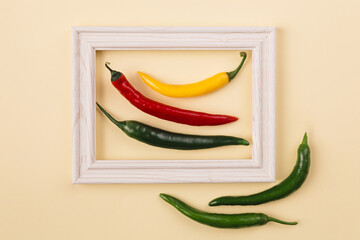 Minimal concept of red, yellow and green pepperoni in the middle of wooden frame with two more papirka's outside against pastel background.  Creative flat lay