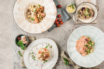 Several plates of fish and seafood pasta served by the chef on a light background.