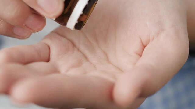 Two big light brown round pills fall into palm of hand from pill bottle. Close-up, front view, center composition