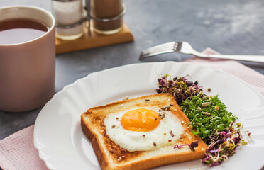 A sandwich with egg in the hole of the bread, microgreens, healthy food Breakfast, a cup of tea