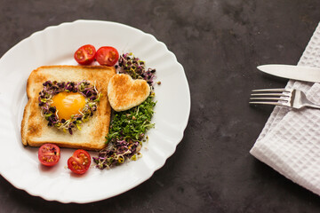 Egg in a hole of bread heart shape, microgreens, healthy food Breakfast, tea, black background