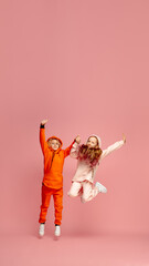 Flyer. Happy children isolated on coral pink studio background. Look happy, cheerful. Copyspace for ad. Childhood, education, emotions, facial expression concept. Jumping high, playing, having fun.