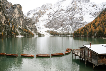 Fototapeta na wymiar snowy landscape with mountains, trees, boats to navigate in the water in the lago di braies. Located in the dolomites, the Italian alps