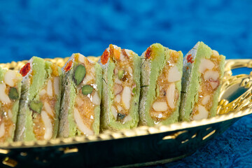 Indian Kaju Diamond Barfi Or Burfi Made Of Dry Fruits Like Badam Almonds Kaaju Mava Powdered Cashew Nuts Pista Kesar Doodh Ghee And Mawa Served In Golden Tray. Turquoise Background And Space For Text