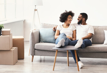African Family Relaxing Among Moving Boxes Sitting On Couch Indoors
