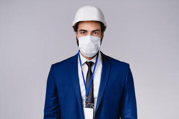 Confident young engineer in hardhat and medical mask against Covid19 isolated over grey background