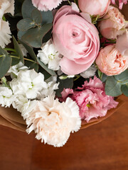 Delicate bouquet of dianthus, rose, ranunculus and eucalyptus in craft paper in the morning light