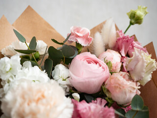 Delicate bouquet of dianthus, rose, ranunculus and eucalyptus in craft paper in the morning light
