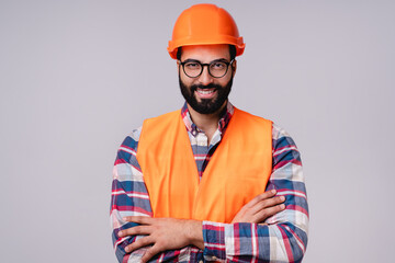 Confident handsome Arabic construction worker in special uniform and hardhat with arms crossed isolated over grey background