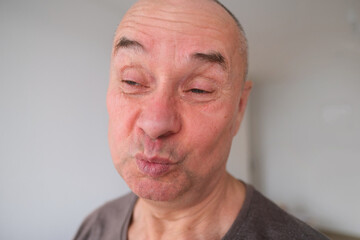 face of a European old man close up, wrinkles on the aging skin, bares teeth, makes grimaces, the concept of mental health, cosmetology, age-related changes