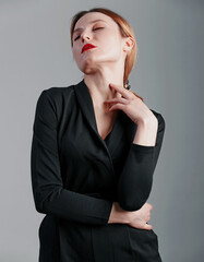 Elegant business woman in black classic jumpsuit posing over gray background.