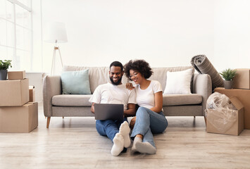 African Couple Using Laptop Sitting On Floor In New Apartment