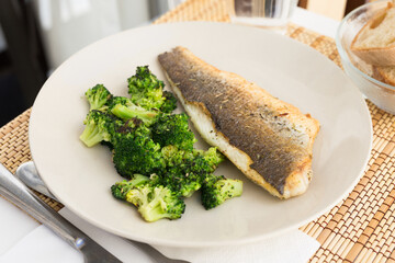 fried fillet of sea bass with garnish of broccoli on black warm stone plate