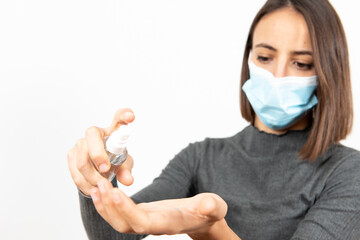 Hispanic girl washing her hands with sanitizing gel while wearing a medical mask. Selective focus on the bottle. Healthcare during Coronavirus pandemic concept.