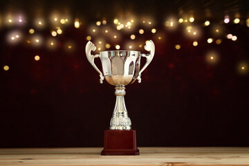 image of gold trophy over wooden table and dark background, with abstract shiny lights