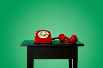 red rotary dial telephone off the hook on a table