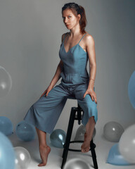 Elegant business woman in classic jumpsuit sitting on a chair surrounded by balloons over gray...