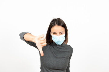 Disgusted latin woman wearing a face mask with the thumbs down. Mental health during Coronavirus pandemic concept.