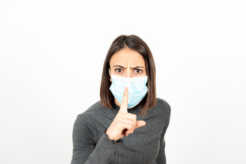 Latin woman commanding silence with the finger on the medical face mask. Healthcare during Coronavirus pandemic concept.