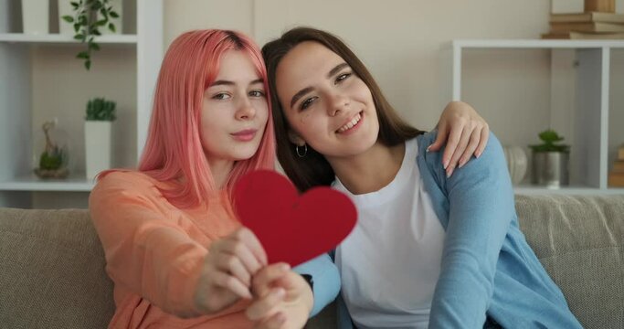 Lesbian couple embracing and holding heart shape paper at home