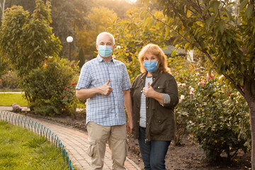 Senior couple wearing masks showing thumbs up