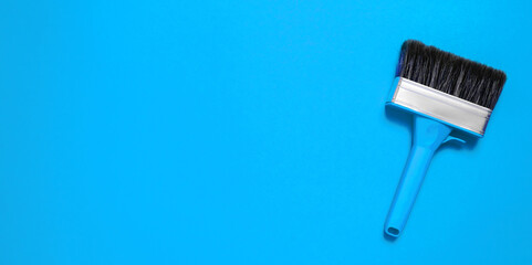 Large new brush in metal edging with plastic handle for construction painting or canvas priming on a blue background. Banner with copy space for a hardware store or art shop. Close-up. Clean bristle