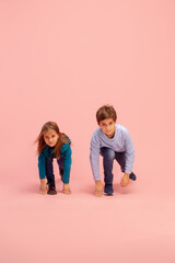 Starting up. Happy children isolated on coral pink studio background. Look happy, cheerful. Copyspace for ad. Childhood, education, emotions, facial expression concept. Having fun, ready to run