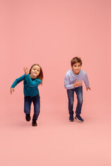 Fototapeta premium Aspiration. Happy children isolated on coral pink studio background. Look happy, cheerful. Copyspace for ad. Childhood, education, emotions, facial expression concept. Having fun, running on