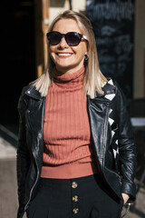 young beautiful smiling stylish blonde woman in sunglasses, black pants and leather jacket posing...